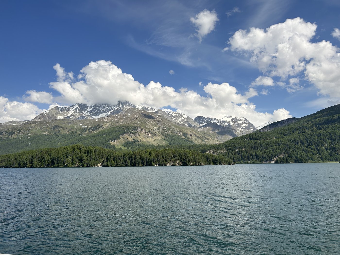 Horské jezero obklopené lesy a zasněženými vrcholy